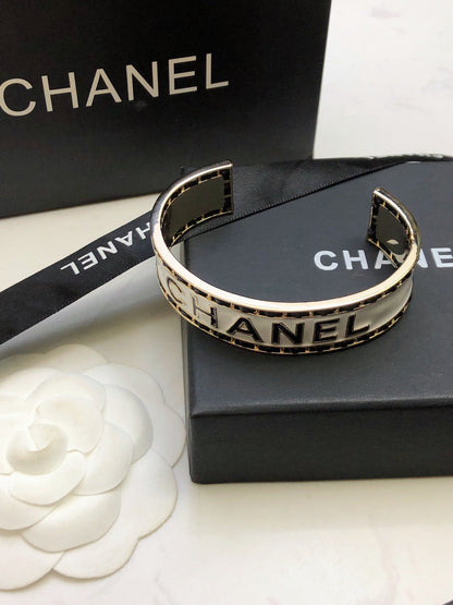 CHANEL 26S CHANEL LOGO ENAMEL CUFF BRACELET WITH BLACK TRIM IN GOLD METAL 630835